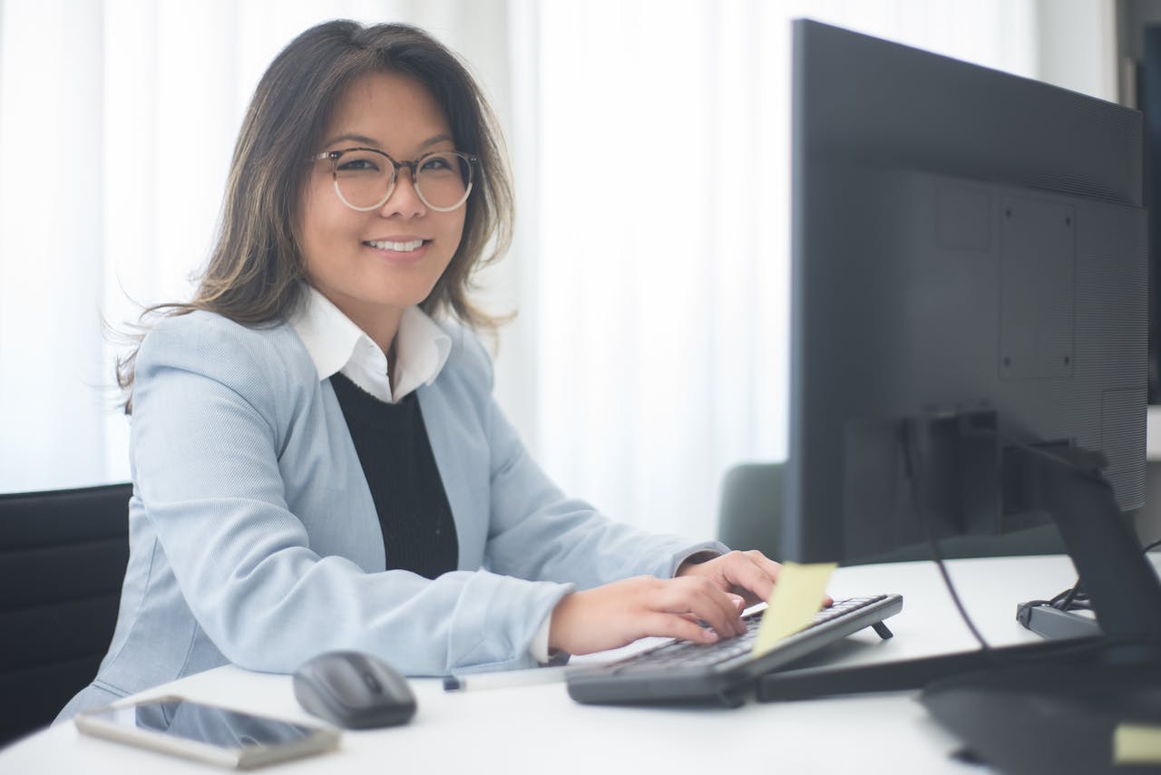 Professional woman smiling while working at a computer in an office setting.