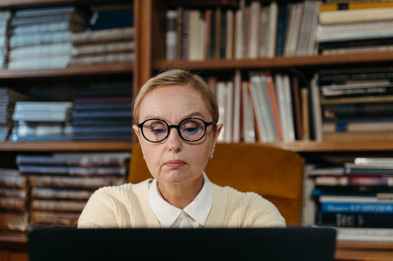 Senior woman with eyeglasses focused on work in a library setting.